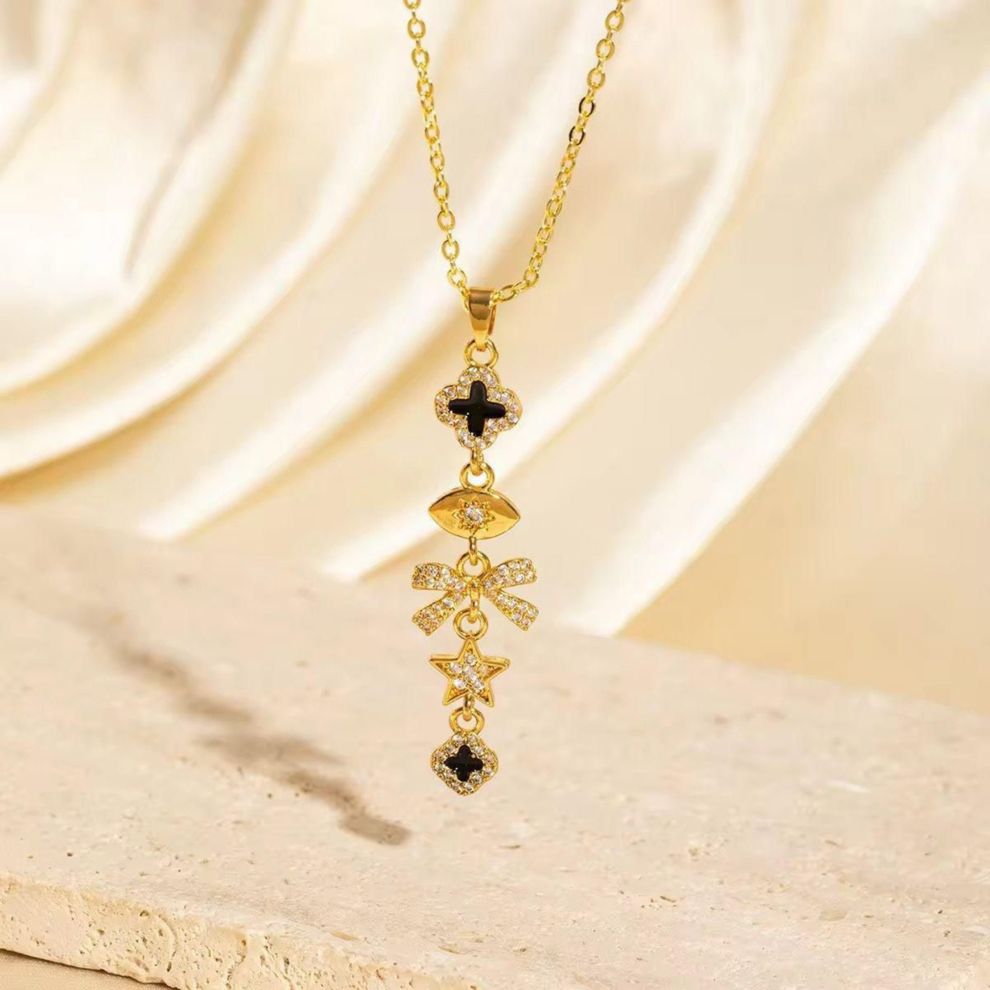 Celestia Noir Charm Necklace in gold tone with black enamel, crystal clover, bow, star and cascading pendant charms by ZARIVA.