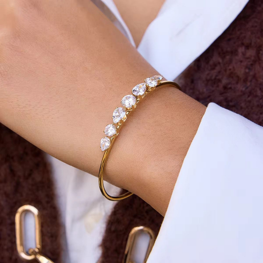 Aurelia tennis bracelet featuring sparkling clear stones on a gold-tone open cuff, styled elegantly on the wrist.