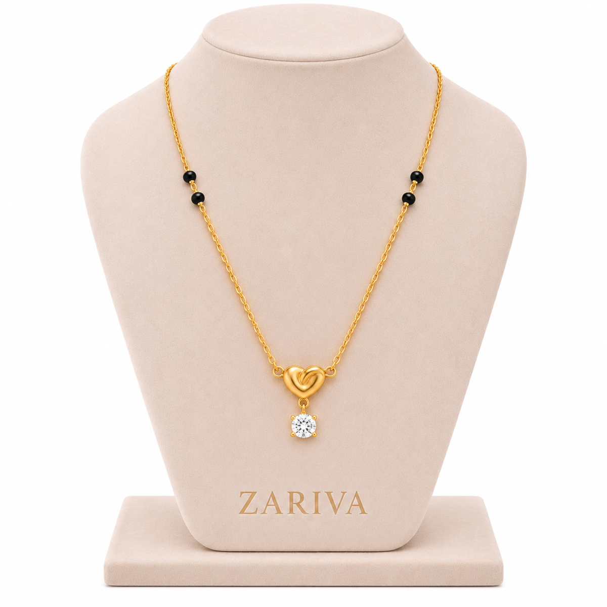 A gold necklace displayed on a beige jewelry bust. The necklace has a gold chain with small black beads and a pendant featuring a gold heart and a clear round gemstone.