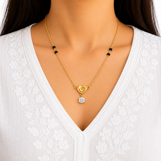 A close-up of a model wearing a delicate gold chain necklace with a heart-shaped pendant and small black beads, paired with a white lace V-neck top.