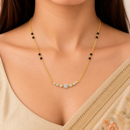 A close-up of a woman wearing a delicate gold necklace with small black beads and a central cluster of clear stones, paired with a beige garment.