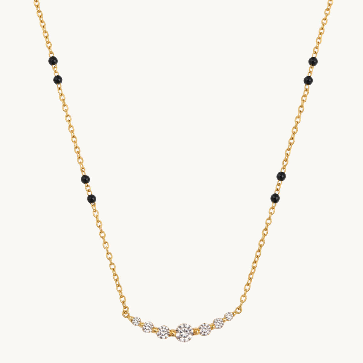 A delicate yellow gold chain necklace featuring small black round beads spaced along the chain and a curved central section set with clear gemstones, photographed on a solid off-white background.