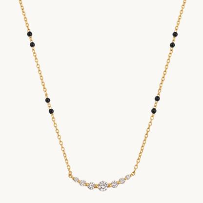 A delicate yellow gold chain necklace featuring small black round beads spaced along the chain and a curved central section set with clear gemstones, photographed on a solid off-white background.