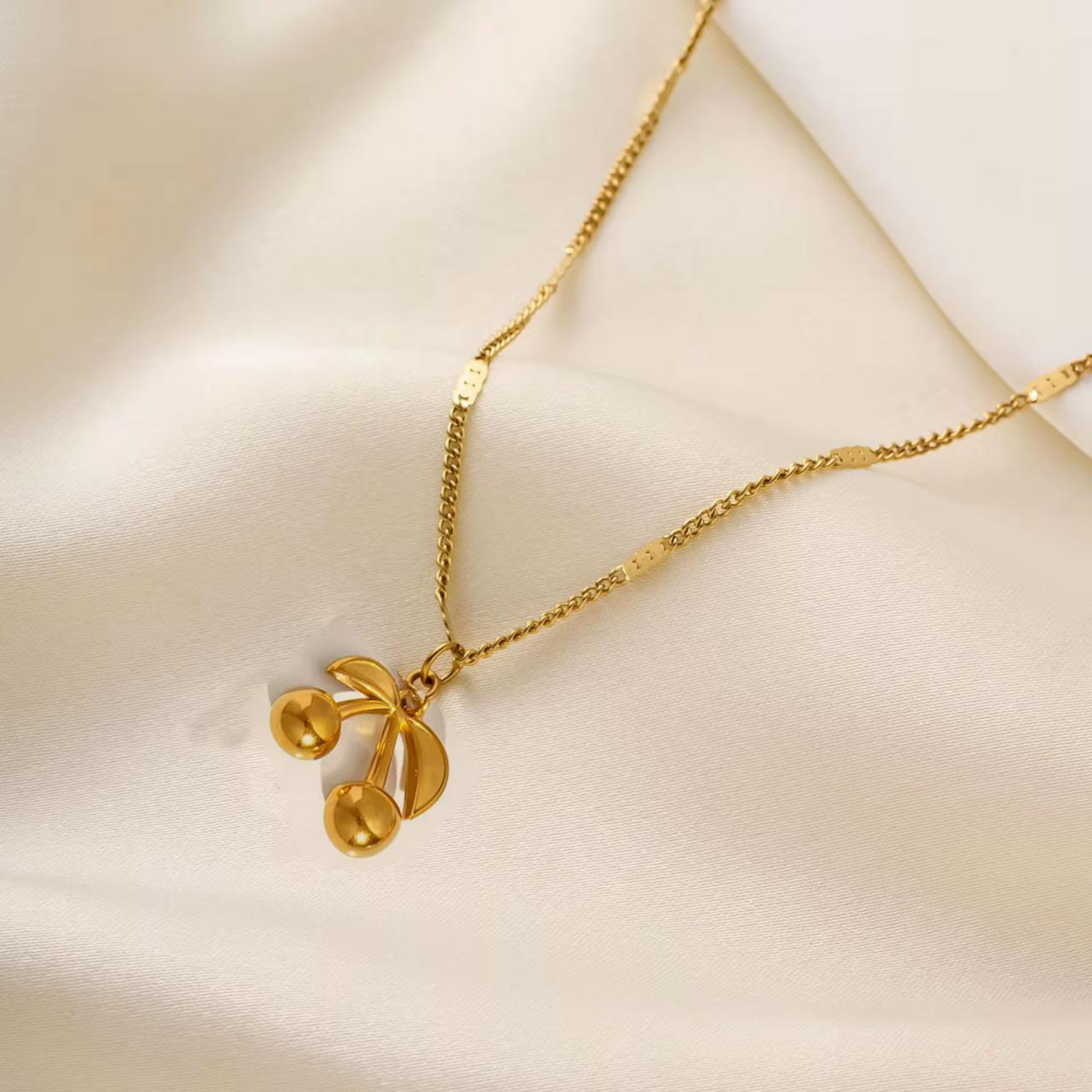 Cherry pendant necklace close-up showing the polished double-cherry pendant, curved leaf accents and delicate gold-tone chain.