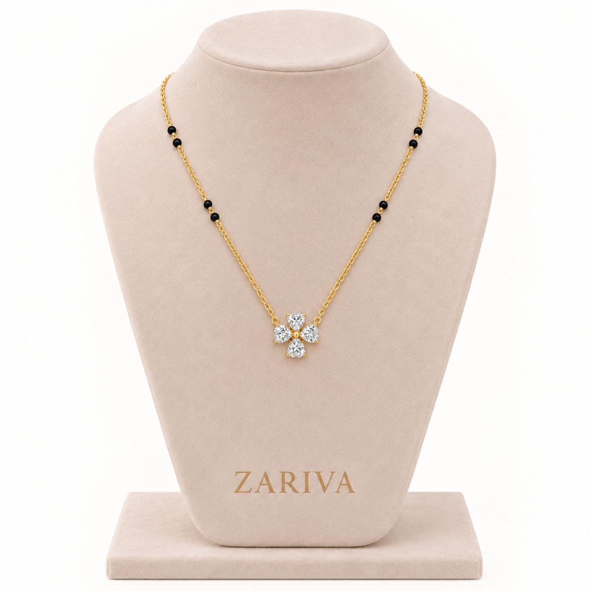 A gold necklace with a four-petal flower pendant set with clear stones, displayed on a beige jewelry bust. The necklace has small black bead accents along the chain.