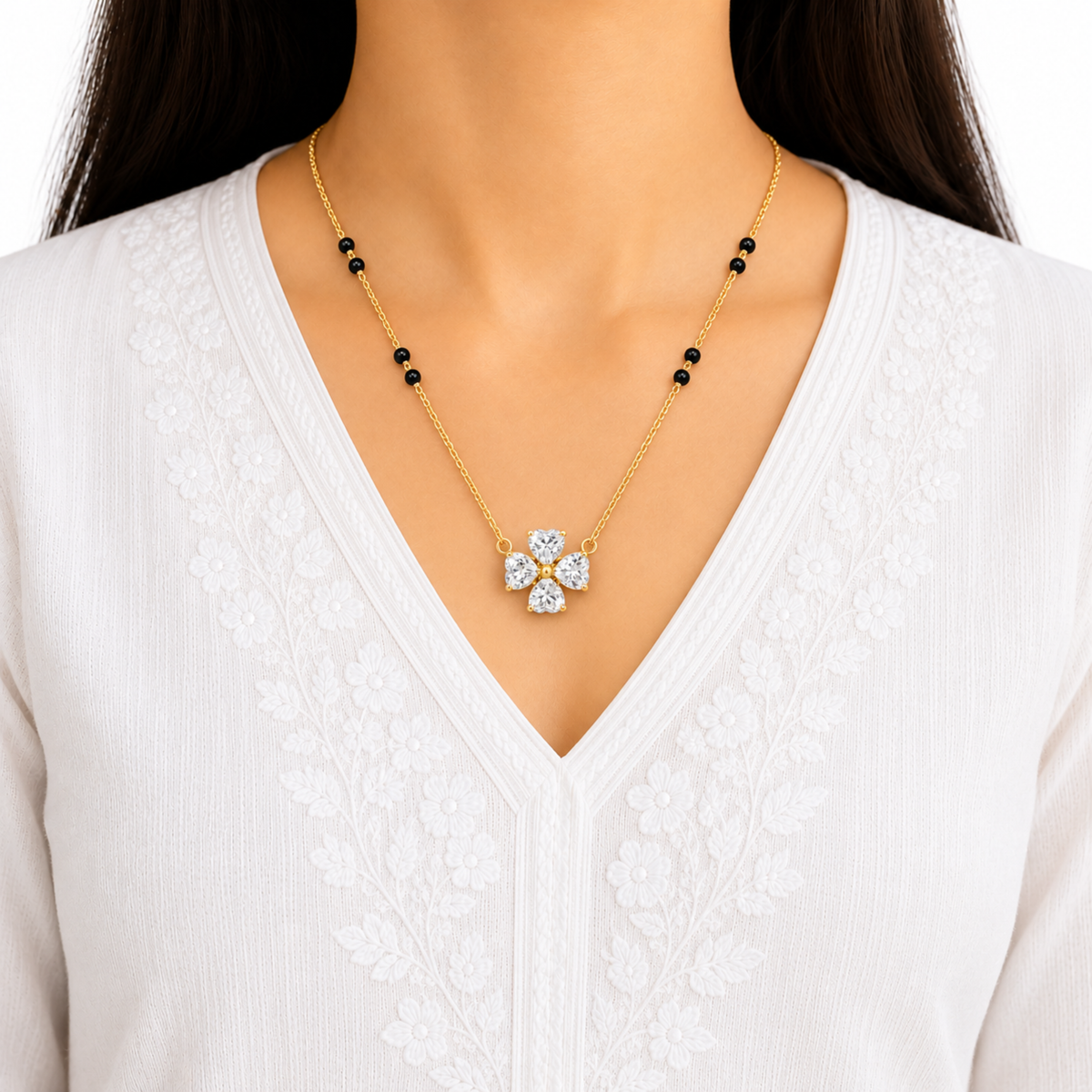 Four-stone clear zircon flower mangalsutra in gold with black beads, styled on a model wearing a white embroidered V-neck outfit by ZARIVA.
