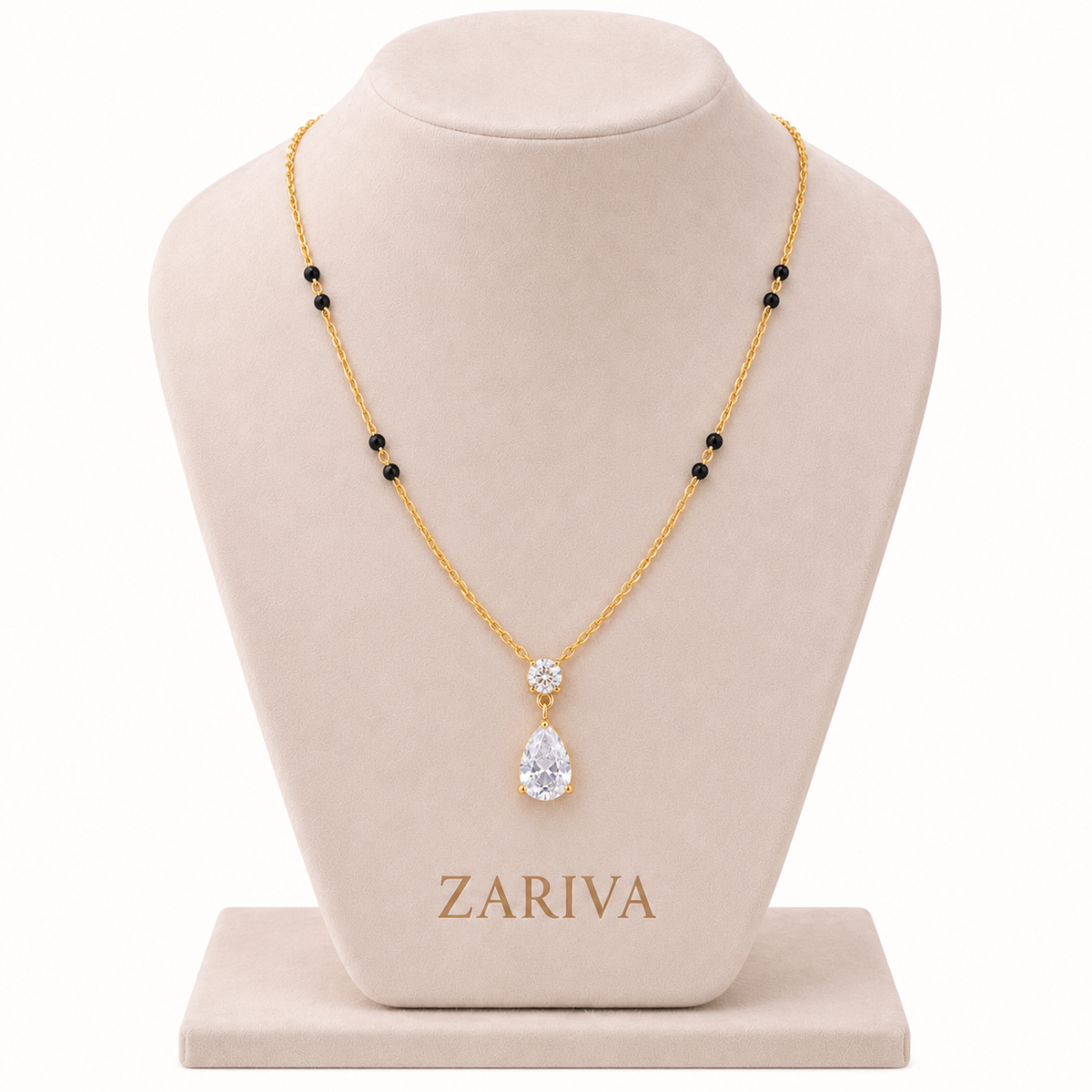 A gold necklace with a teardrop-shaped clear gemstone pendant and a small clear stone above it, displayed on a beige jewelry bust. The necklace has small black bead accents spaced along the chain.