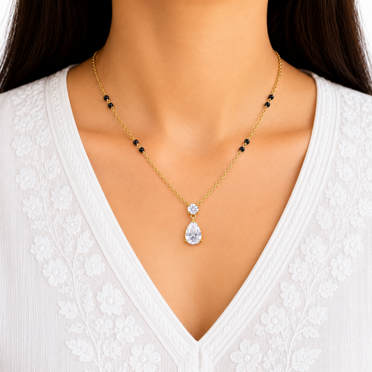 Gold mangalsutra necklace with black bead accents and a teardrop zircon pendant worn with a white embroidered kurta.