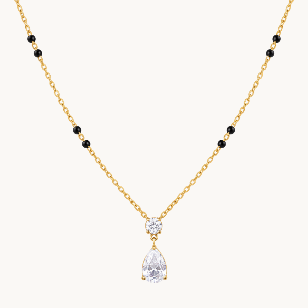 Close-up of a gold mangalsutra pendant featuring a round clear zircon above a pear-shaped teardrop stone with gold settings.