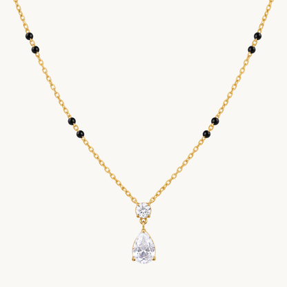 Close-up of a gold mangalsutra pendant featuring a round clear zircon above a pear-shaped teardrop stone with gold settings.