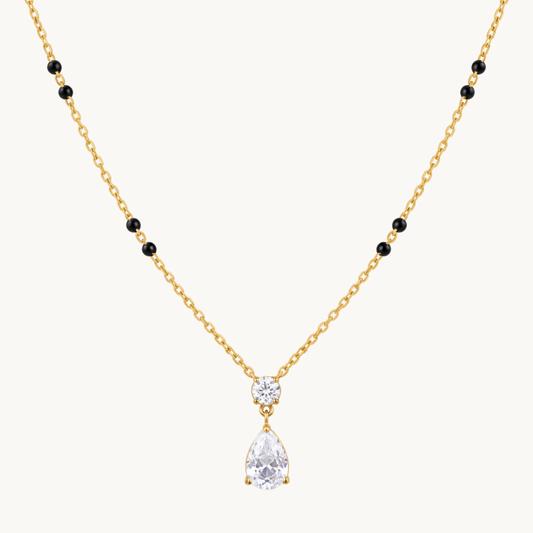 Close-up of a gold mangalsutra pendant featuring a round clear zircon above a pear-shaped teardrop stone with gold settings.