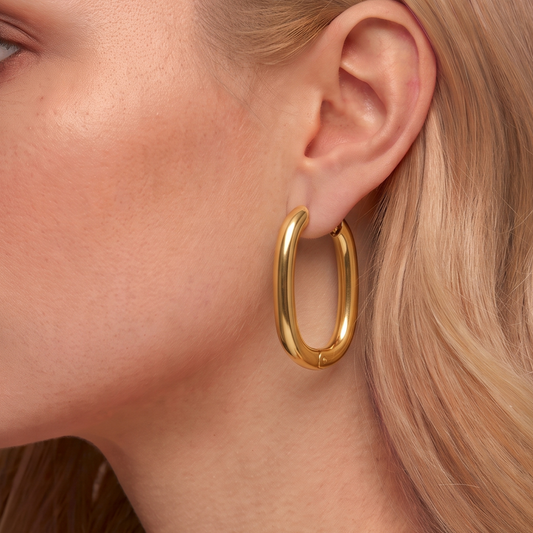 Gold oval hoop earrings worn on the ear, highlighting the elongated curved silhouette and polished contemporary design by ZARIVA.