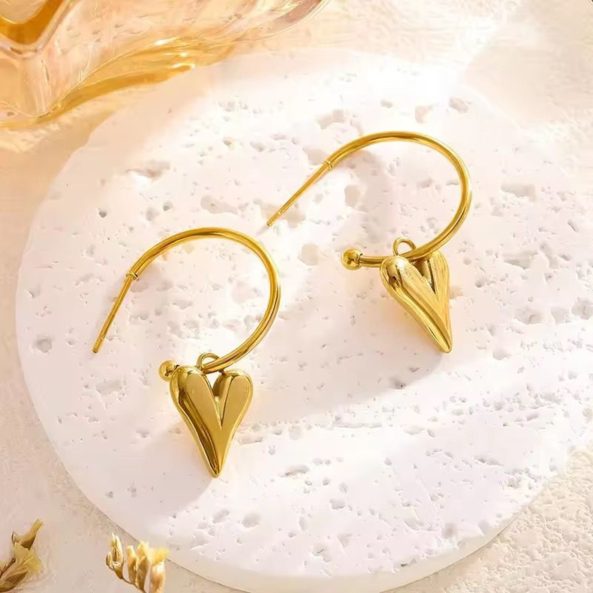 Gold heart earrings displayed on a textured surface, highlighting the polished heart drop design and contemporary jewellery style by ZARIVA.