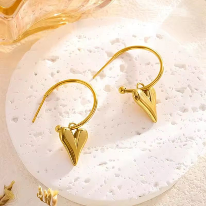 Gold heart earrings displayed on a textured surface, highlighting the polished heart drop design and contemporary jewellery style by ZARIVA.