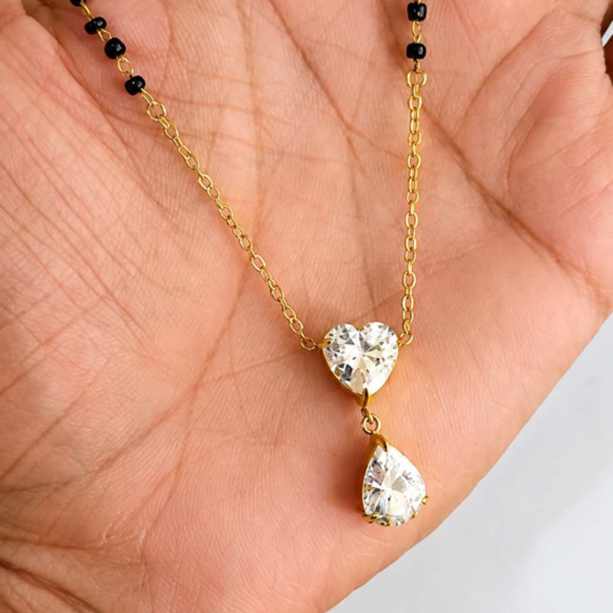 ZARIVA mangalsutra close-up showing the heart-shaped cubic zirconia pendant, teardrop drop and black bead detailing.
