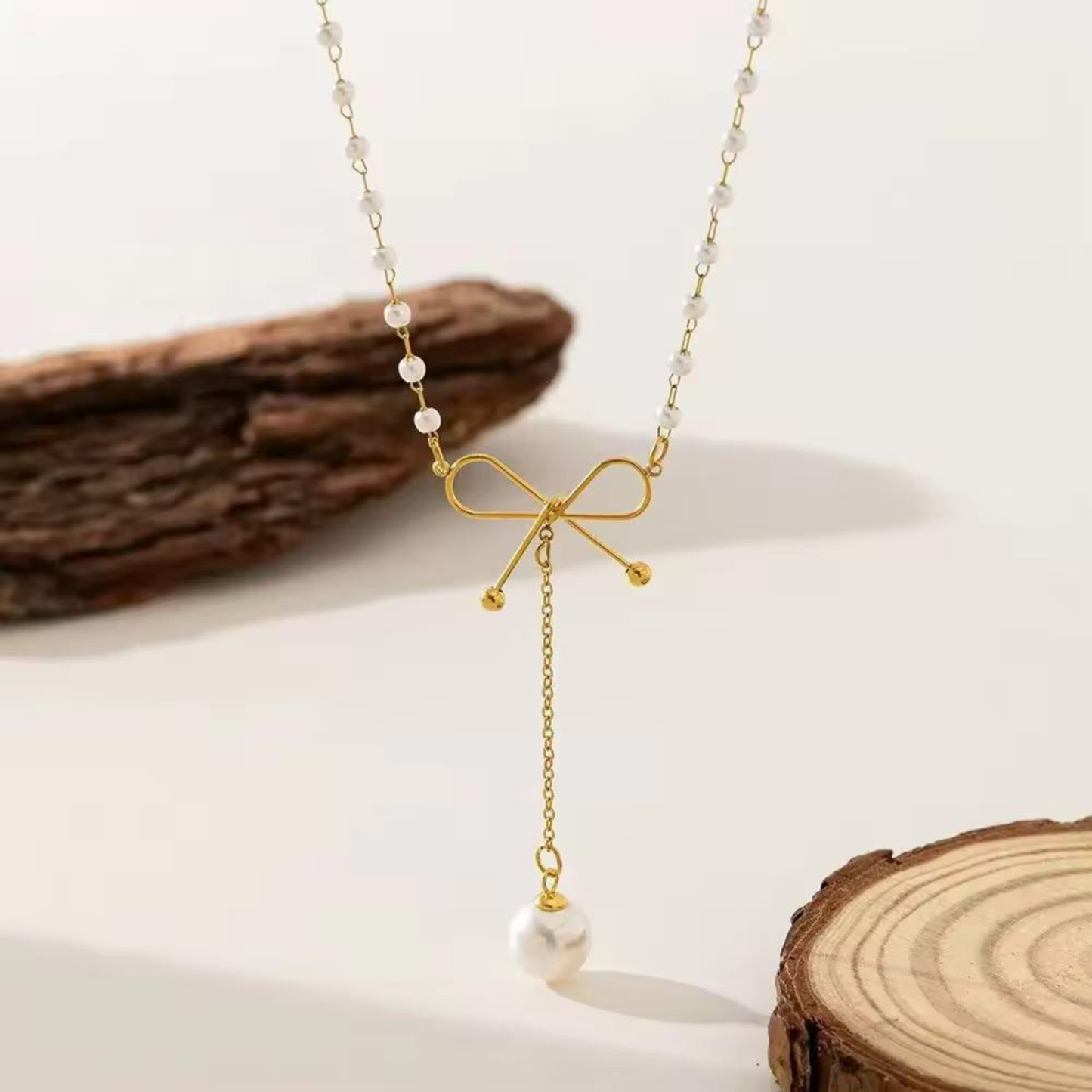 Pearl Bow Necklace styled with a gold bow centerpiece, pearl chain and dangling white pearl charm in an elegant setting