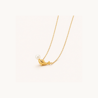 Pearl dolphin pendant necklace displayed on a soft neutral background, highlighting its gold finish, delicate chain and pearl detail.