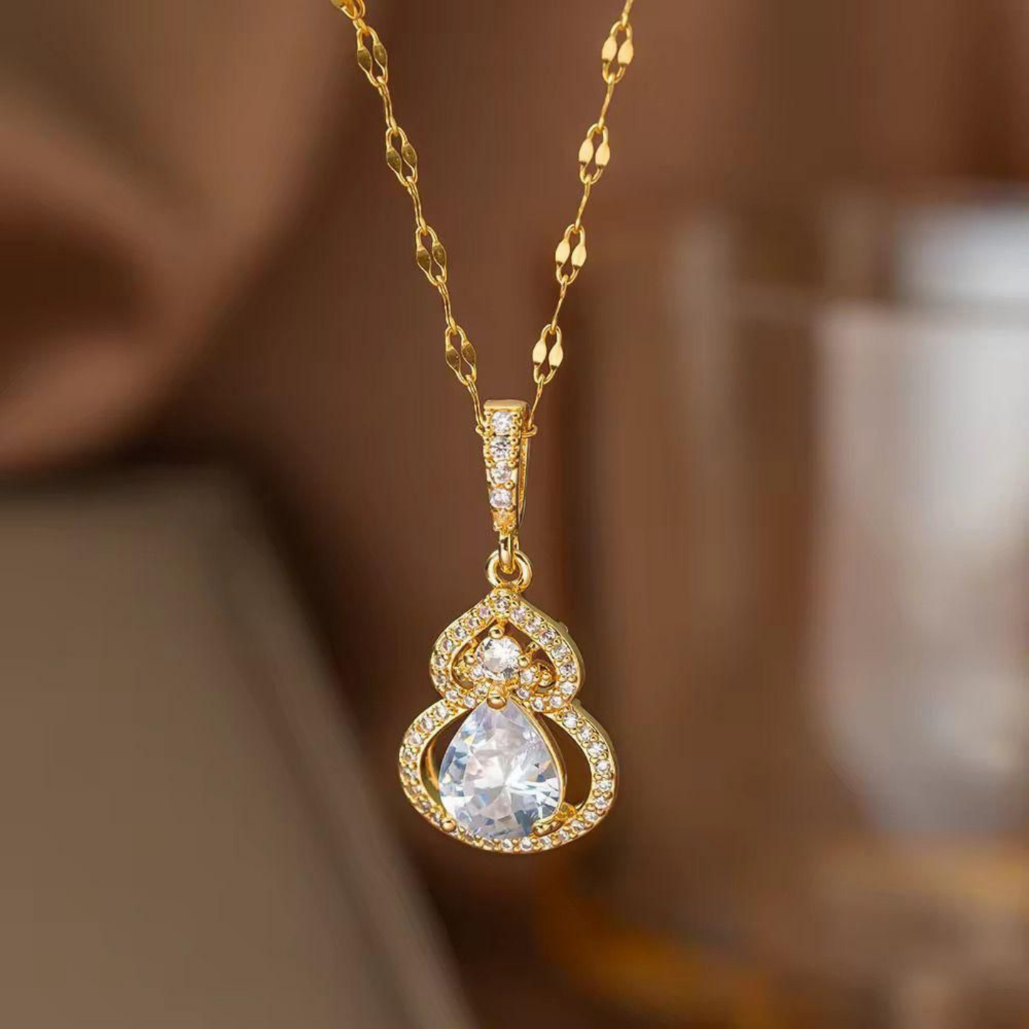 Teardrop pendant necklace featuring a large clear pear-cut stone, sparkling halo accents, and a gold-toned decorative chain.