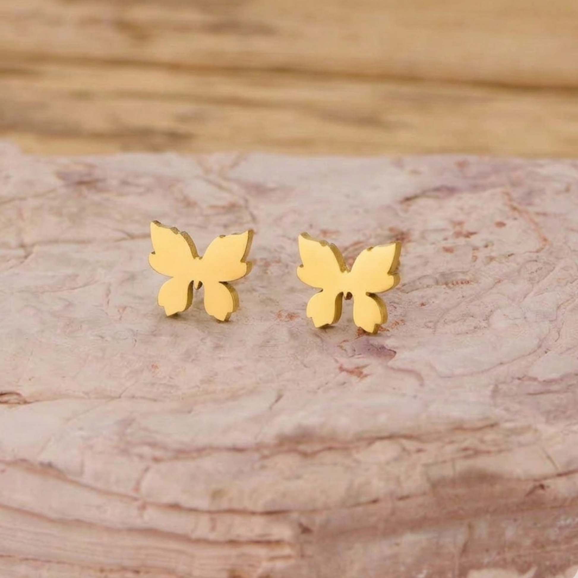ZARIVA Mariposa Mini Butterfly Stud Earrings displayed on a natural stone surface. Premium SS316L stainless steel earrings with 18K PVD gold plating, anti-tarnish finish and elegant butterfly design.